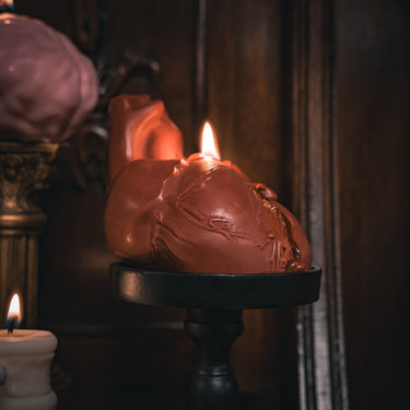 Heart-shaped candle on a stand with a lit candle in the background